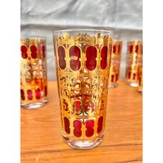 four red and gold glasses sitting on top of a wooden table