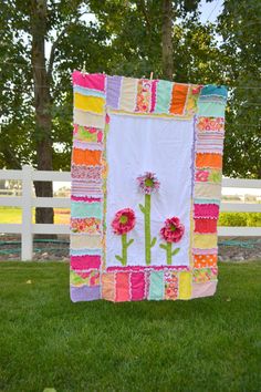 a colorful quilt hanging on the side of a white fence