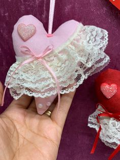 a hand holding a pink heart ornament next to two red hearts on a purple background