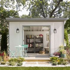 a small white shed sitting in the middle of a yard with a table and chairs