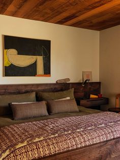 a large bed sitting under a painting on top of a wooden wall next to a night stand