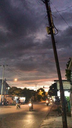 the sky is dark and cloudy as people ride their motorcycles down the street at night