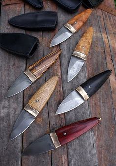 several knives are laid out on a wooden table next to leather wallets and knife sheaths