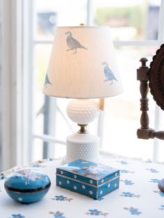 a lamp sitting on top of a table next to a blue box and a clock