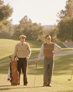 two men are standing on the golf course with their bags and putters in hand