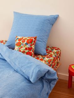 a bed with two pillows and a blue blanket on it next to a red table