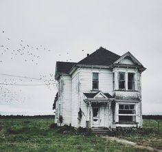 an old white house with birds flying in the air above it and grass on the ground