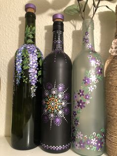 three wine bottles with flowers painted on them are lined up next to a basket and vase