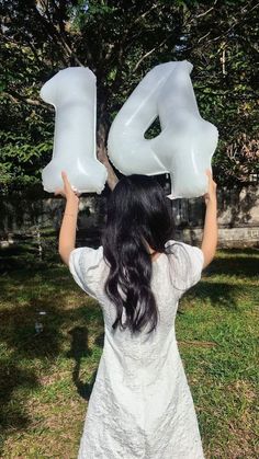 a woman holding two large white balloons in the shape of numbers 4 and 4 on her head