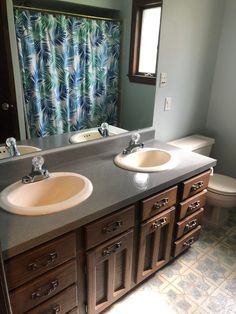 a bathroom with two sinks, a toilet and a shower curtain in the window area