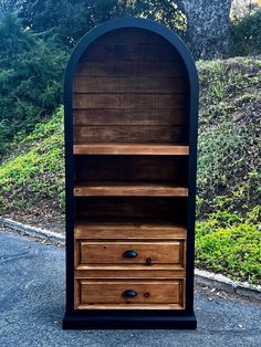 an old fashioned wooden bookcase sitting on the side of a road in front of some trees