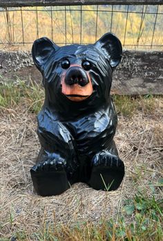 a black bear statue sitting on the ground in front of a caged area with grass