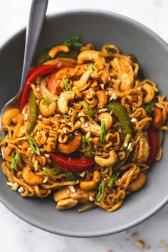 a bowl filled with noodles and vegetables on top of a white countertop next to a silver spoon