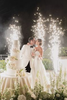 a newly married couple kissing in front of their wedding cake with fireworks coming from behind them