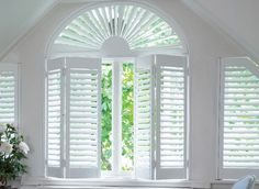 an arched window with white shutters and flowers in the vase on the table next to it