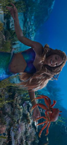 a beautiful young woman in a blue and green mermaid costume standing under water with crabs