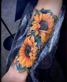 a sunflower tattoo on the arm with leaves and flowers around it's center