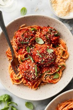 two bowls filled with spaghetti and meatballs on top of a marble countertop next to other dishes