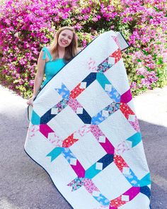 a woman holding up a quilt in front of flowers