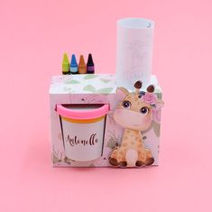 a giraffe shaped box with crayons next to it on a pink background