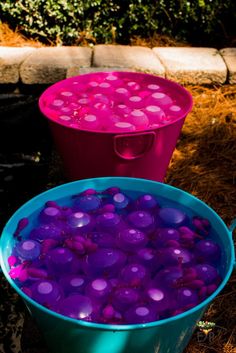 two buckets filled with purple and pink liquid sitting on the ground next to each other