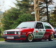 a red and white car parked on the side of a road next to some trees