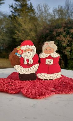 santa and mrs claus are sitting on a red rug with trees in the back ground