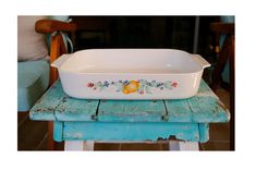 a white casserole dish sitting on top of a blue wooden table next to a chair