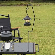 a camping table with two lights on it in the middle of a grassy field next to a lawn chair