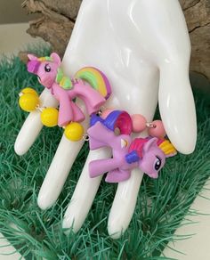 three little pony figurines sitting on top of green grass next to a fake hand