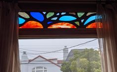 an open window with a view of the street and houses through it's curtains