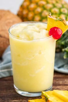 a pineapple drink in a glass next to sliced pineapples and other fruit