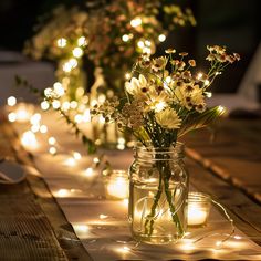 mason jar filled with flowers sitting on top of a wooden table covered in fairy lights