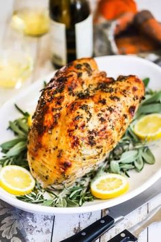 a white plate topped with chicken covered in herbs and lemons next to a bottle of wine