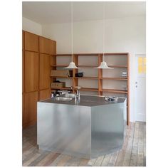 a kitchen with an island in the middle and wooden shelves behind it, along with two hanging lights