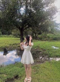 a woman in a white dress is standing by a tree and looking up at the sky