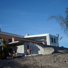 an unfinished house sits on the side of a hill next to a palm tree in front of it