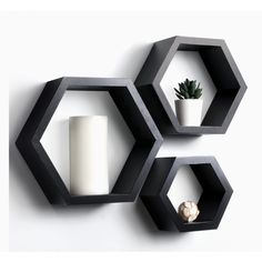 three black hexagonal shelves with two white candles and a succulent plant