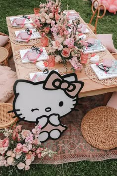 a hello kitty table set up with pink flowers and place settings for an outdoor party