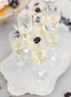 small glasses filled with champagne and berries on a white tray next to other desserts