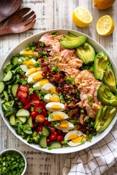 a large salad with hard boiled eggs, avocado and tomatoes in a white bowl