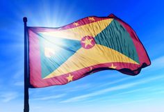 a flag flying in the wind on a sunny day with blue sky and sun behind it