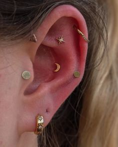 a close up of a person's ear with three stars and moon piercings