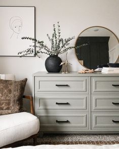 a dresser with a mirror and vase on it in a room that has white walls