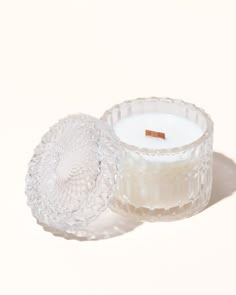 a clear glass candle with a wooden stick sticking out of it's top sitting on a white surface