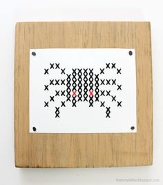 a cross - stitch pattern on a wooden frame with metal studs and red dots