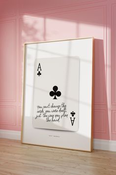 a frame with a playing card on it in front of a pink wall and wooden floor