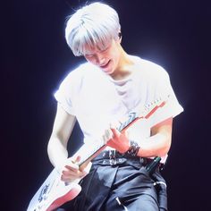 a male in a white shirt and black pants is playing an electric guitar on stage