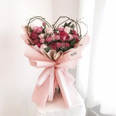 a bouquet of pink roses in a heart - shaped vase on a white pedestal next to a window