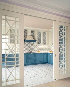 an open kitchen with blue cabinets and white tile flooring on the walls is seen through glass doors